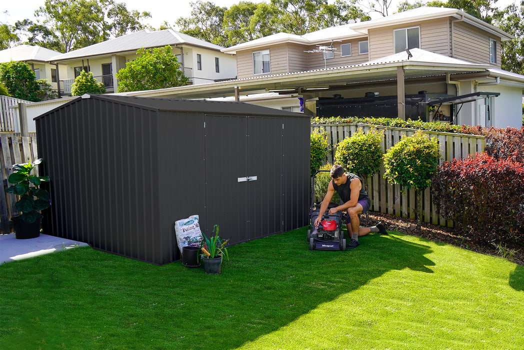 A man with lawnmower beside the Absco Premier 10 ft Metal Outdoor Storage Monument Shed.