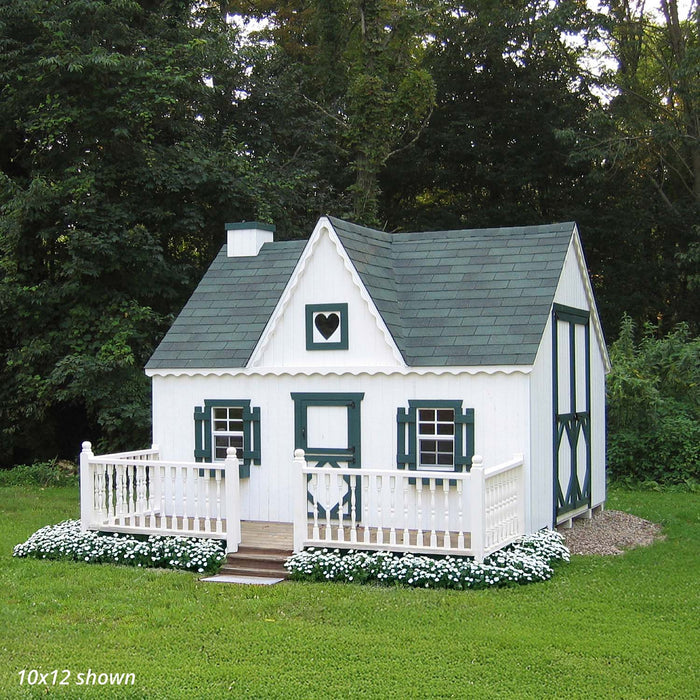 White 10x12 Victorian Playhouse with green shutters and trim, surrounded by lush grass and trees, showcasing the charming backyard setup.