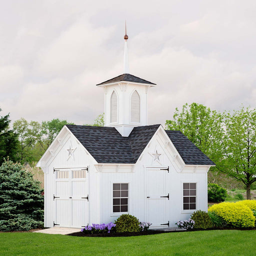 10x14 Little Cottage Co. Star Barn with white wood siding, black roof shingles, copper-tipped spire, and decorative star vents surrounded by garden greenery.