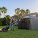 Man with a lawn mower next to the Lifetime 10x8 ft. storage shed, palm trees in the background.