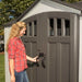 Woman opening the side entry doors of the Lifetime 10x8 ft. storage shed, showing built-in door windows.