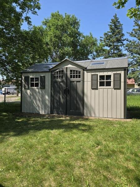 Lifetime 15x8 ft. storage shed installed in a grassy yard, front angle view with closed doors.