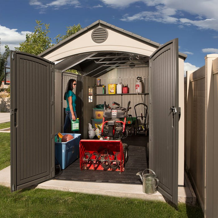 Interior view of the Lifetime 15x8 ft. storage shed with open door showing a mower, snowblower, and shelving.