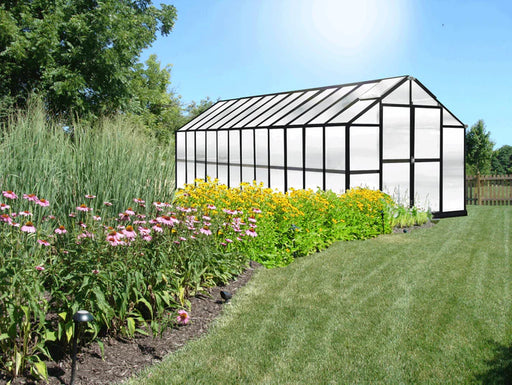 Large 24 ft Growers Supply greenhouse with durable black frame and polycarbonate panels beside vibrant flower beds