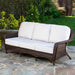 The Tortuga Outdoor Sea Pines 6-Piece Outdoor Wicker Sofa Set in Java, featuring white cushions, sits on a stone patio amid greenery and lawn—perfect for relaxing with stylish Tortuga Outdoor furniture.