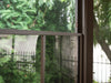 Interior view through the mesh screen of Gazebo 12x12 Florence Solarium showing the garden and fence outside.