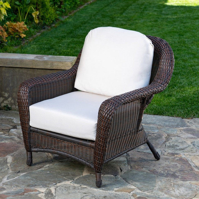 The Tortuga Outdoor Sea Pines 6-Piece Outdoor Wicker Sofa Set in Java features white cushions on a stone patio, creating an inviting space with grass and greenery in the background.