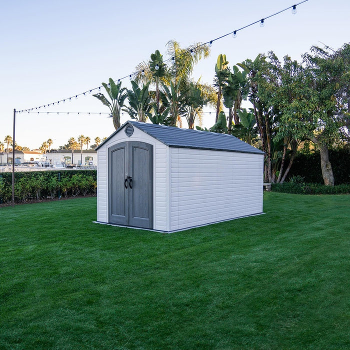 Angled view of the Lifetime 8 Ft. x 15 Ft. Outdoor Storage Shed in a backyard, highlighting its placement on grass with a garden background.