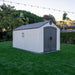 Side view of the Lifetime 8 Ft. x 15 Ft. Outdoor Storage Shed on a green lawn with garden and string lights in the background.