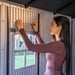A woman installing or adjusting the window latch inside the Lifetime 8 Ft. x 15 Ft. Outdoor Storage Shed.