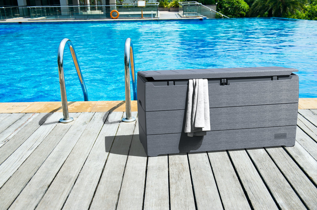 Duramax 270 Liter Outdoor Storage Box in Gray with a towel on it, located on a wooden pool deck.