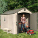 Man with a lawn mower next to the Lifetime 8x12.5 ft. storage shed with open doors and a ladder stored inside.