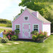 Pink 8x12 Gingerbread Cottage Playhouse by Little Cottage Co. with scalloped trim, white Dutch door, and heart window surrounded by blooming garden.