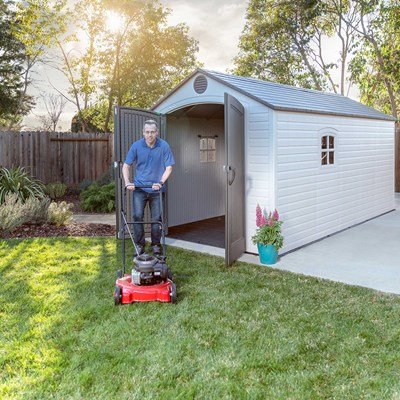 Man with a lawn mower next to the Lifetime 8x15 ft. storage shed with one door open.