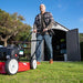 Man mowing the lawn in front of the Lifetime 8x15 ft. outdoor storage shed with open doors.