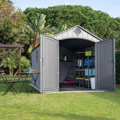 Woman wheeling a bike into the Lifetime 8x15 ft. storage shed with open doors, mower and totes stored inside.