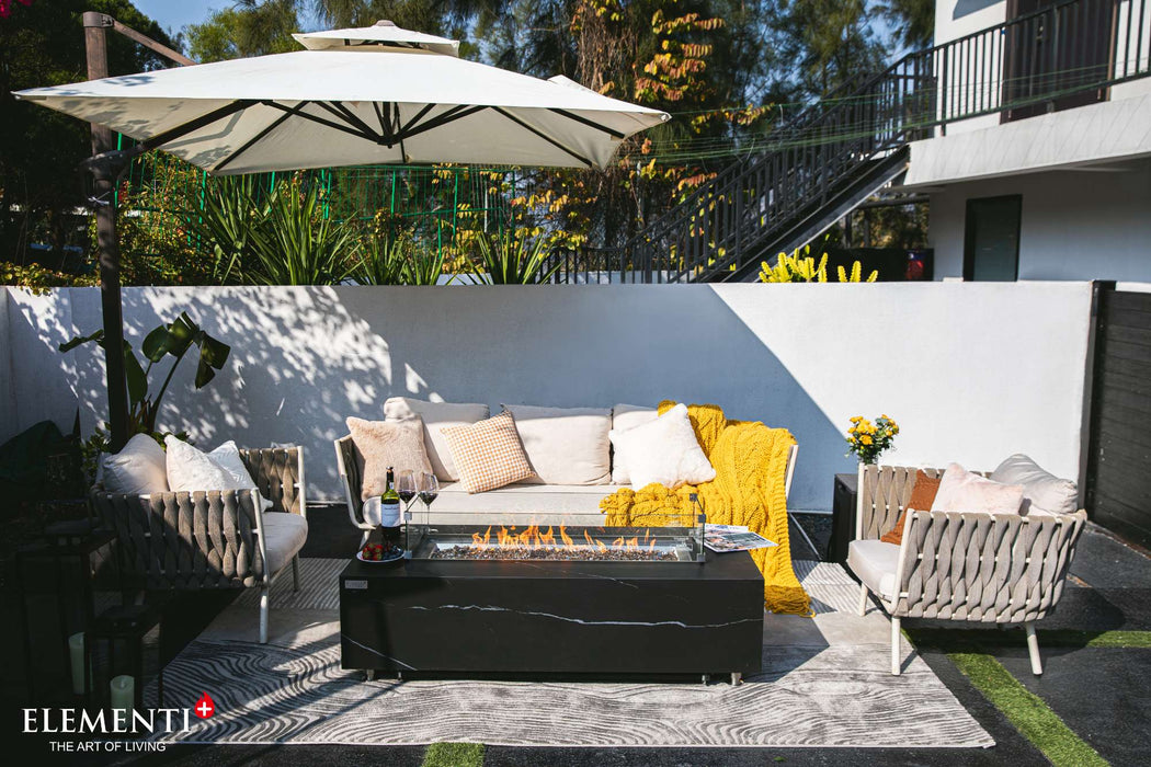 A patio featuring a white umbrella and couches, complemented by the Elementi Plus Varna Marble Porcelain Fire Table