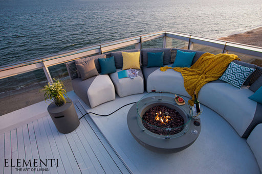 A round OFG101 Lunar Bowl fire pit table with a wind guard, situated on a deck with a stunning ocean view