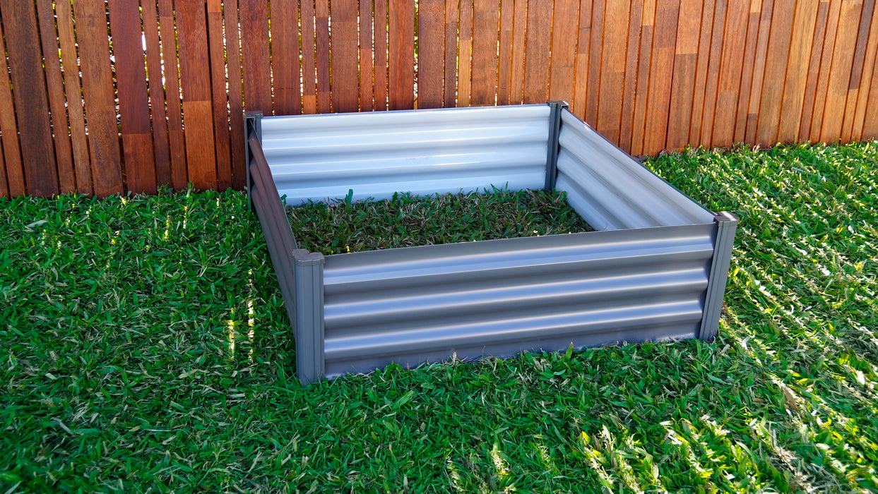 Absco 4x4ft Raised Garden Bed assembled and empty, set against a wooden fence and grass background.