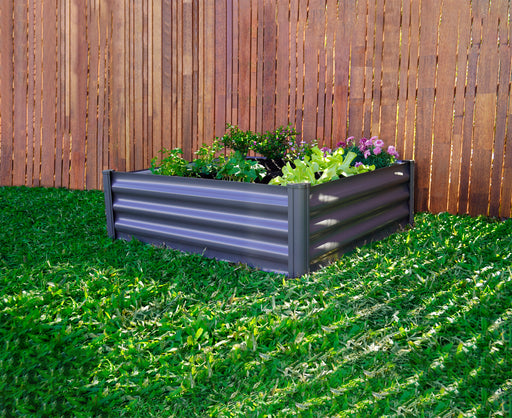 Absco Metal Square Garden Bed filled with a variety of plants, positioned against an old wooden fence.