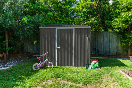 Front view of the Absco  7.5' x 5' Single Door Metal Garden Shed in Woodland Gray placed in a backyard with kid's bicycle and tools outside.