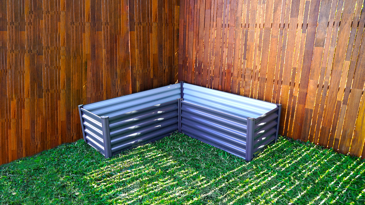 Empty Absco Metal L Garden Bed set up on grass with wooden fence background.