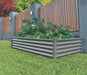 Absco 6' x 3' The Organic Garden Co Metal Rectangle Garden Bed set up in a garden, surrounded by grass and a wooden fence.