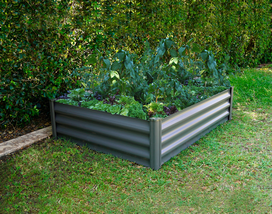 Absco 4x3ft The Organic Garden Co Metal Rectangle Garden Bed in an outdoor setting filled with lush greenery and vegetables, complemented by a natural backdrop of dense shrubs.