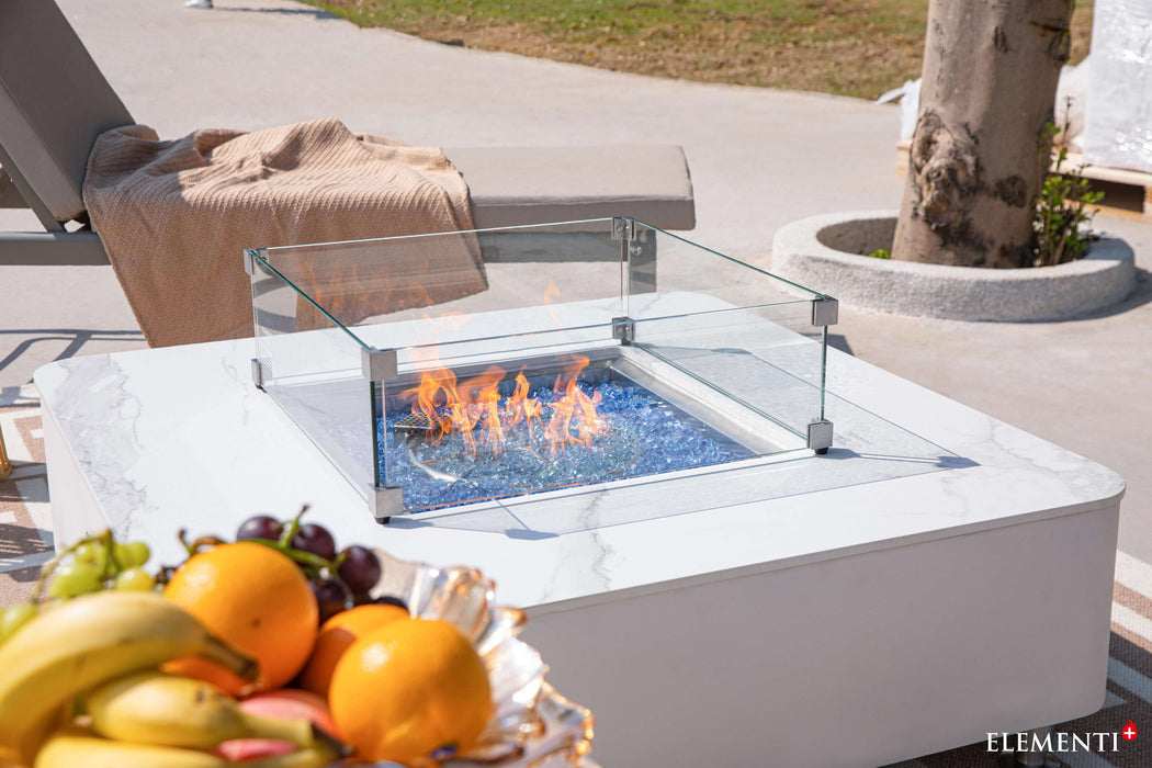 The Elementi Plus Annecy Porcelain Top Fire Table on a patio, accompanied by an assortment of colorful fruit