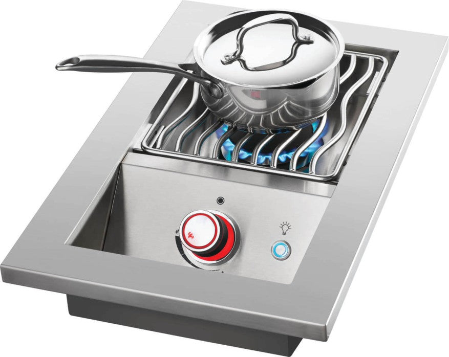 Featuring a lit burner with blue flames under a silver pan, a red-accented control knob in the foreground, and a stainless steel cover on the side.