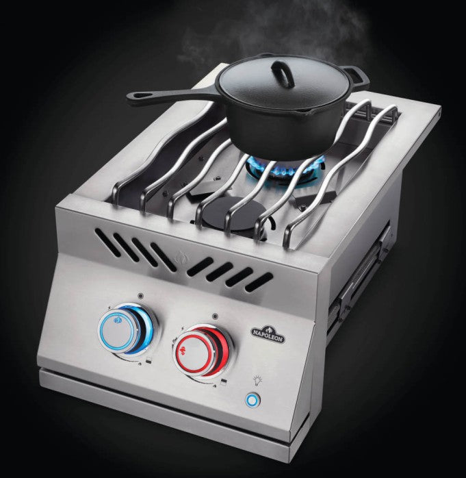 Featuring a lit burner with blue flames under a silver pan, a red-accented control knob in the foreground, and a stainless steel cover on the side.