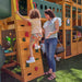 Kid climbing with the help of an adult on the wooden swing set