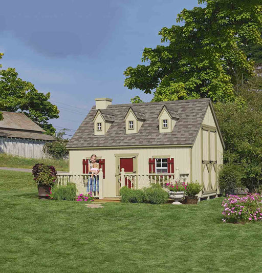 A charming beige Cape Cod Playhouse by Little Cottage Company with red shutters and flower boxes, set in a lush garden.
