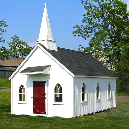 A quaint Little Cottage Chapel Playhouse with a white steeple and red doors, nestled in a green pastoral setting with a clear blue sky overhead.