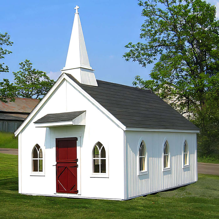 A quaint Little Cottage Chapel Playhouse with a white steeple and red doors, nestled in a green pastoral setting with a clear blue sky overhead.