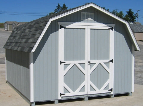 The front view of a Classic Gambrel Barn Kit with white double doors, ready for assembly, showcased on a concrete surface.