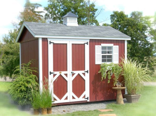A charming Classic Garden Shed by Little Cottage Company with a red facade, white trims, and a cupola, nestled in a lush backyard garden.
