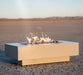 The Outdoor Plus 60" Rectangular Coronado Fire Pit in powder-coated metal, ignited and displayed on a desert-like ground