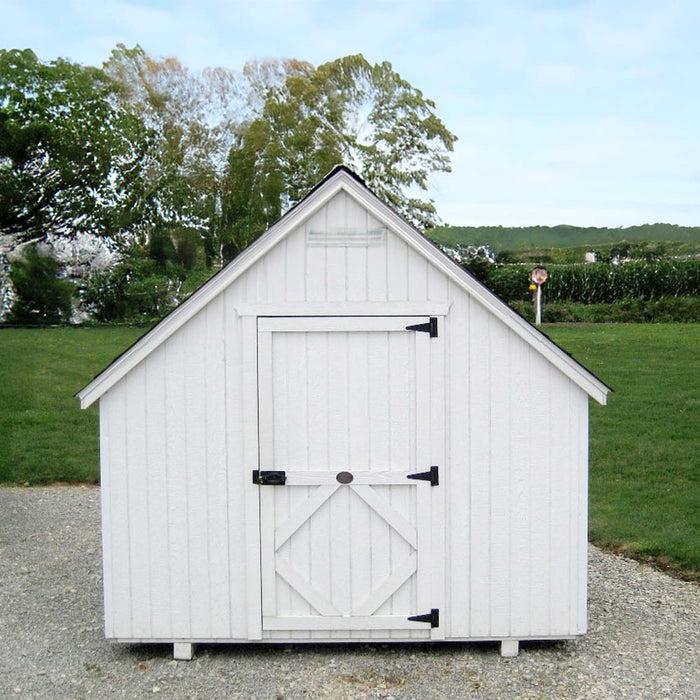 The front view of a Little Cottage Chapel Playhouse, displaying simple white architecture with a cross on the peak, set against a rural backdrop.