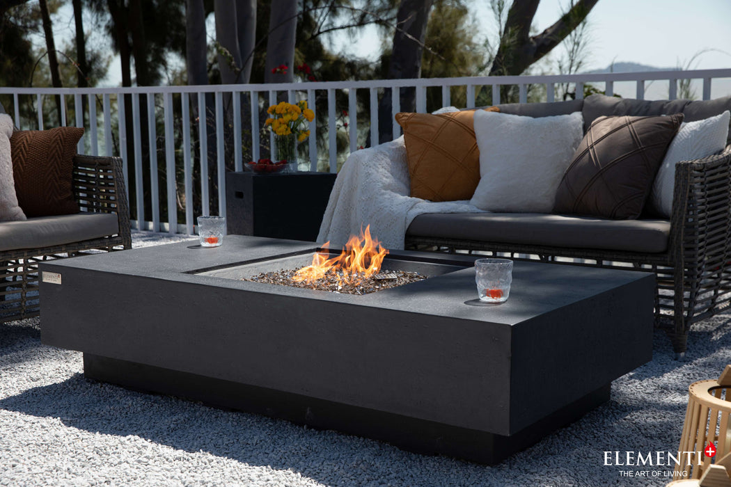 A stylish patio scene showcasing a Dark Grey Cannes Fire Table with inviting chairs arranged around a warm fire pit