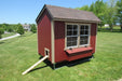 A spacious 5x8 red chicken coop by EZ-Fit, set in a lush green backyard, with a side ramp and windowed exterior.