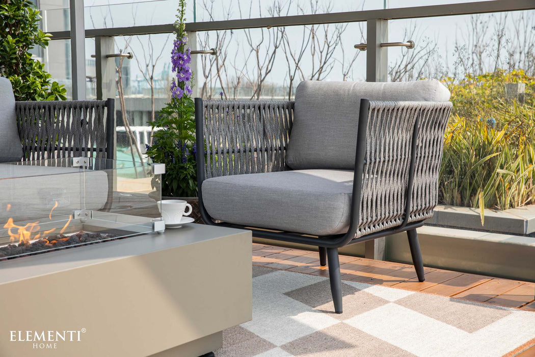 A comfortable chair from the Milano Collection by Elementi Outdoor Furnitures paired with a lit fire pit table, ideal for cozy outdoor evenings.