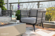A comfortable chair from the Milano Collection by Elementi Outdoor Furnitures paired with a lit fire pit table, ideal for cozy outdoor evenings.