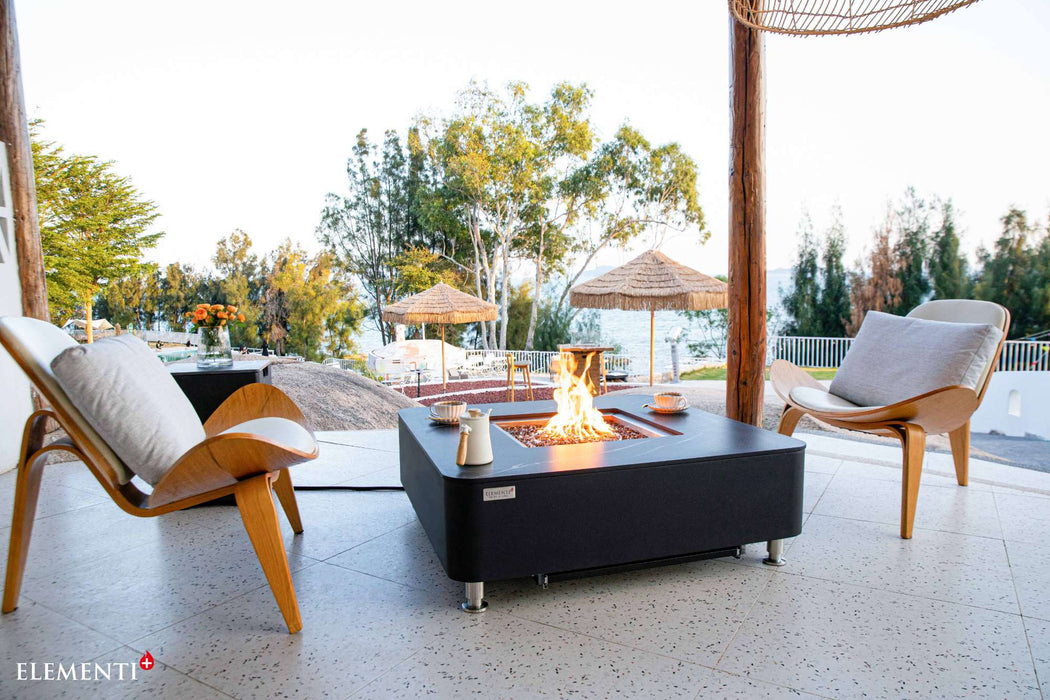 A stylish fire pit on a patio, surrounded by chairs, featuring the Elementi Plus Copenhagen Marble Porcelain Fire Table