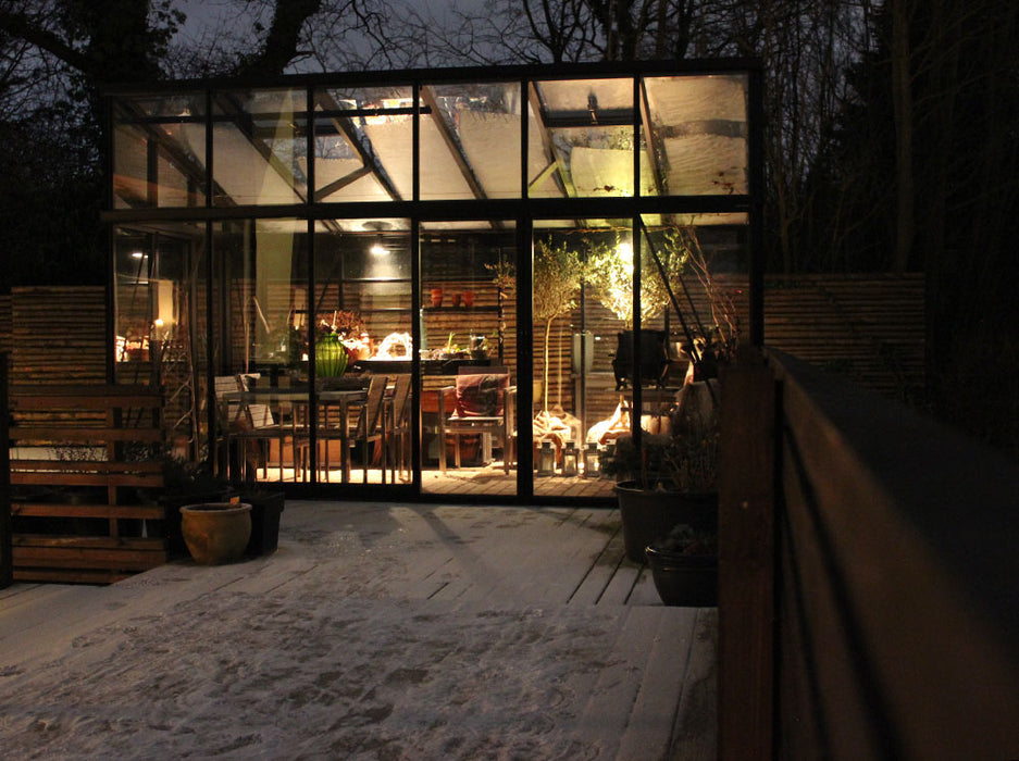 The Exaco Janssens Modern Greenhouse creates a warm refuge on a snowy night, with interior lighting casting a cozy glow on the wintry surroundings.