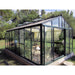 Elegant large Exaco Janssens Royal Victorian VI 46 Greenhouse featuring a robust black frame, expansive clear glass panels, and an ornate ridge cresting, nestled in a verdant garden setting.