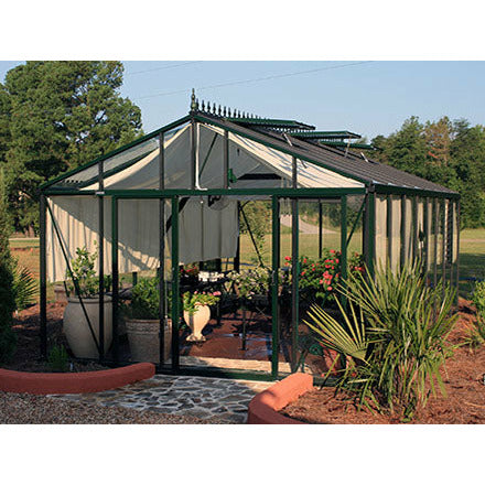 An Exaco Janssens Royal Victorian VI 46 Greenhouse stands elegantly with its green frame amidst a vibrant landscape with red flowers and a cobblestone path.