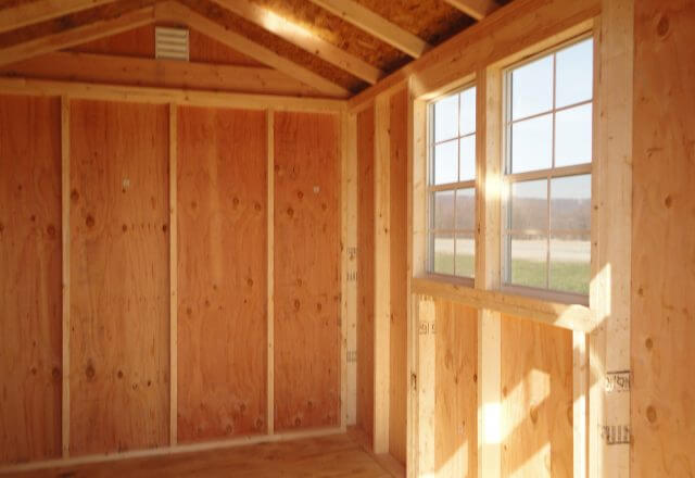 Sunlight streams through the window of the Little Cottage Company's Classic Gable Shed, illuminating the sturdy wooden interior.