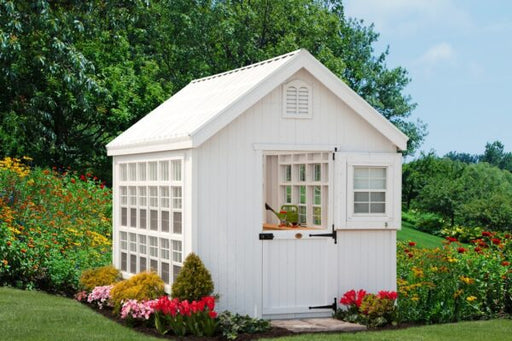 Pristine white Colonial Gable Greenhouse by Little Cottage Company nestled in a lush garden.