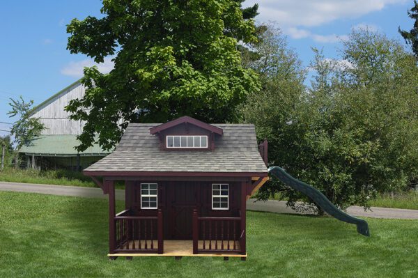 A charming Craftsman Playhouse with Slide by Little Cottage Company, nestled amidst lush green grass, surrounded by towering trees beside a peaceful country road.